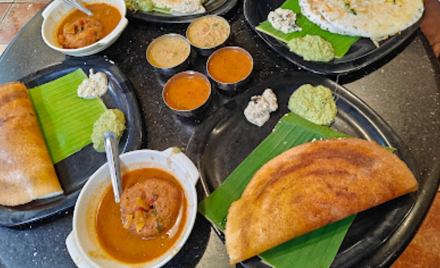 Assortment of **home-style South Indian tiffin** items, including crispy **dosa**, **vada**, sambar, and chutneys, delivered by **Bangalore tiffin services**
